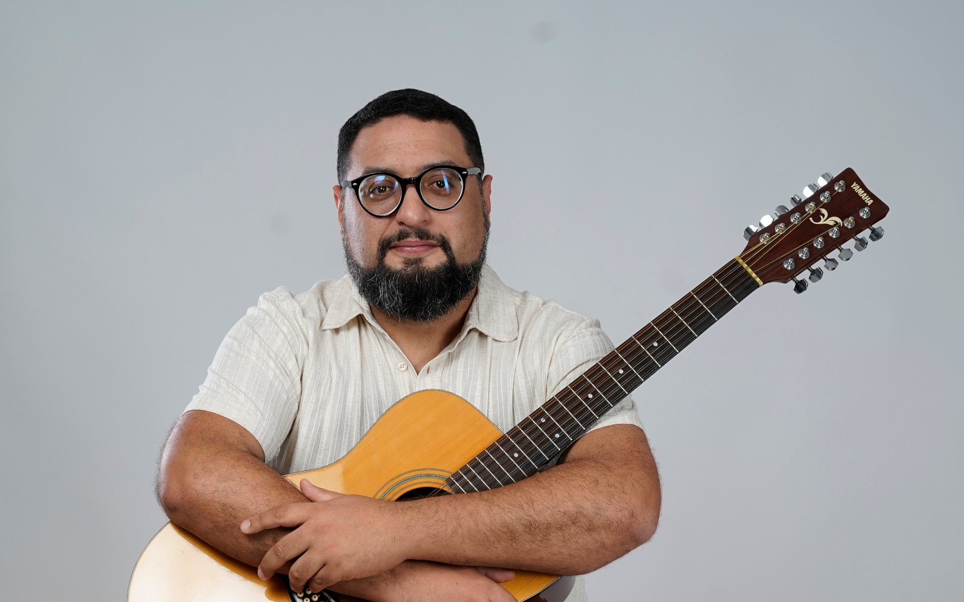 Liêve Ferreira tocando guitarra modelo ES-335 vermelha sentado em um banco contra um fundo branco